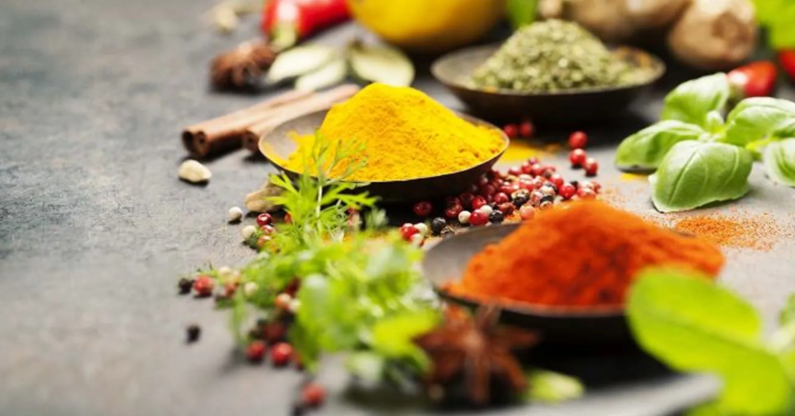 Bowls of turmeric, paprika and dried herbs with peppercorns, cinnamon and fresh basil.